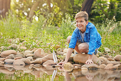 Buy stock photo Shot of a young boy playing with a toy boat by the water