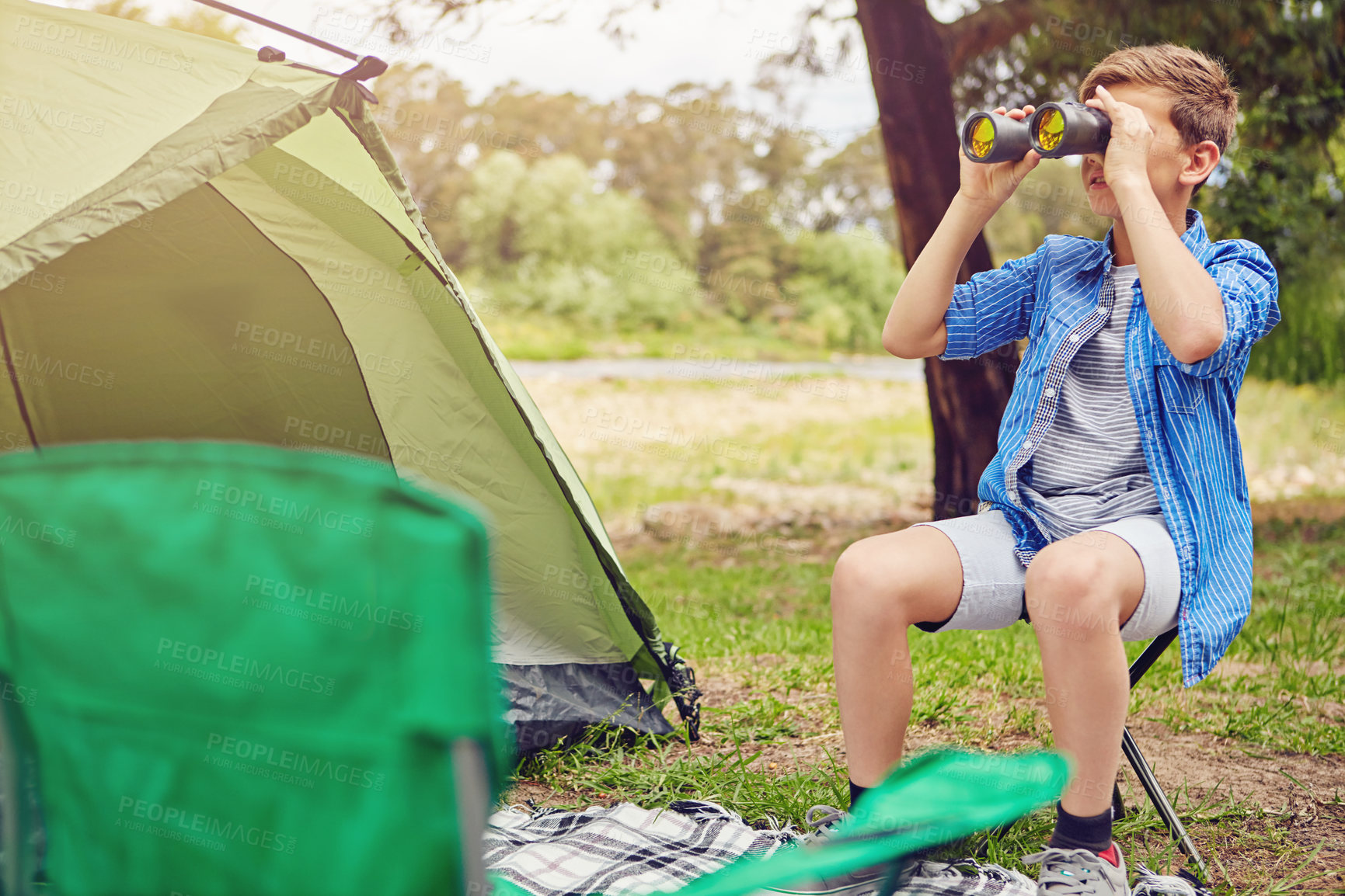 Buy stock photo Shot of a young boy looking through his binoculars at his campsite