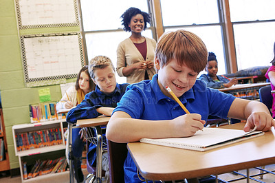 Buy stock photo Shot of a young boy sitting in class with his teacher and classmates blurred in the background