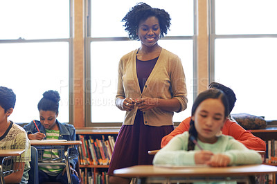 Buy stock photo Shot of a group of elementary children writing a test while a teacher observes