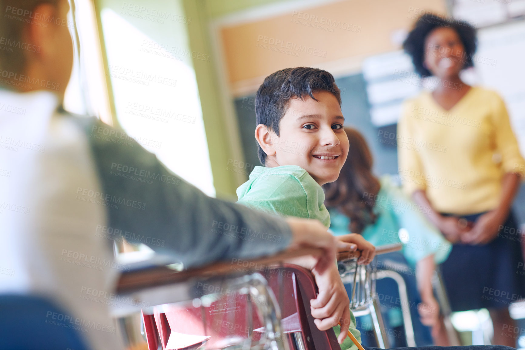 Buy stock photo Shot of a young boy sitting in class with his teacher and classmates blurred in the background