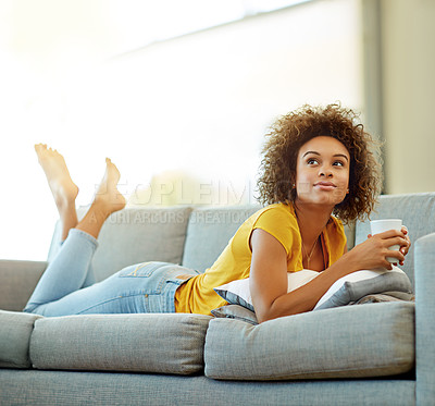 Buy stock photo Shot of a thoughtful young woman relaxing with a warm beverage at home
