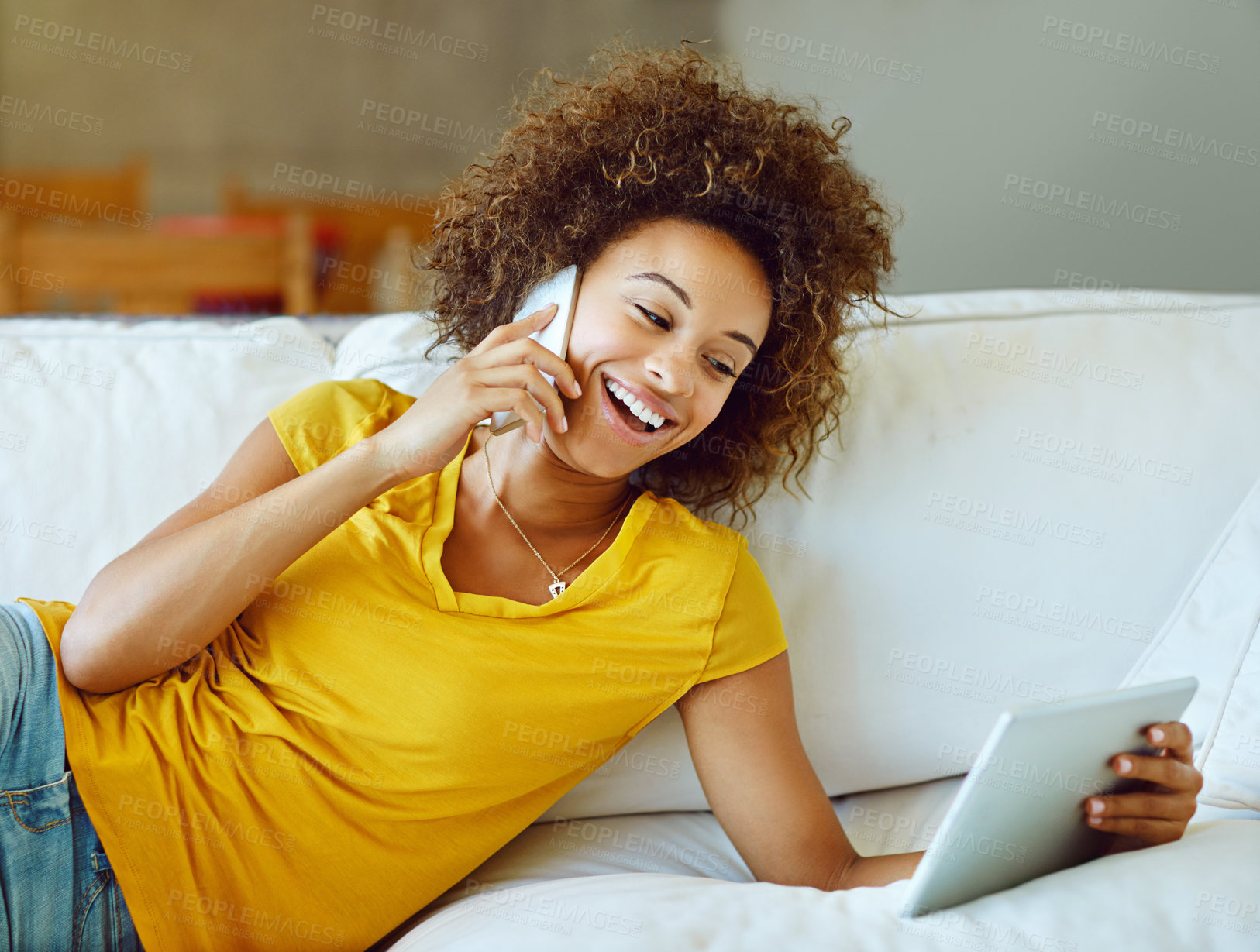 Buy stock photo Shot of a young woman talking on her phone while using a digital tablet on a relaxing day at home