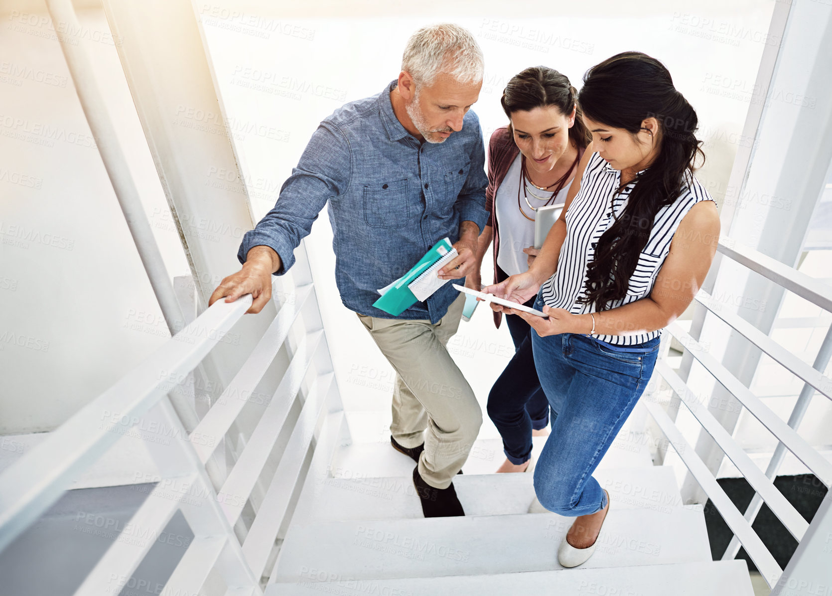 Buy stock photo High angle shot of three colleagues looking at a digital tablet