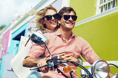 Buy stock photo Shot of a young couple riding a scooter through colorful city streets