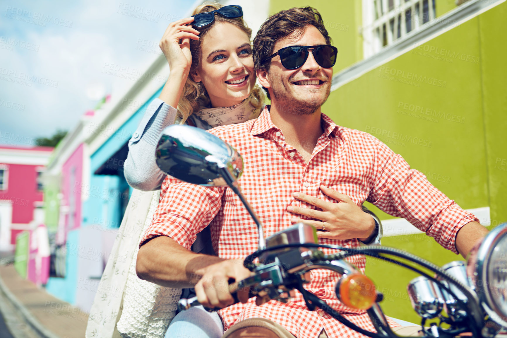 Buy stock photo Shot of a young couple riding a scooter through colorful city streets