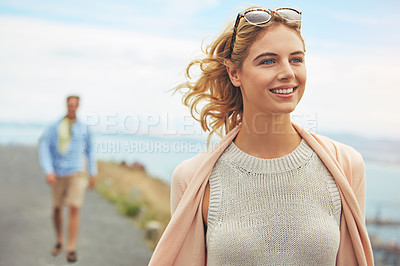 Buy stock photo Shot of a young woman walking outdoors with her boyfriend blurred in the background