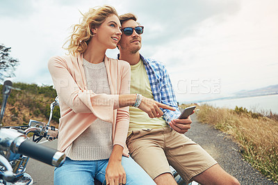 Buy stock photo Shot of a couple using a cellphone while taking a break from their road trip
