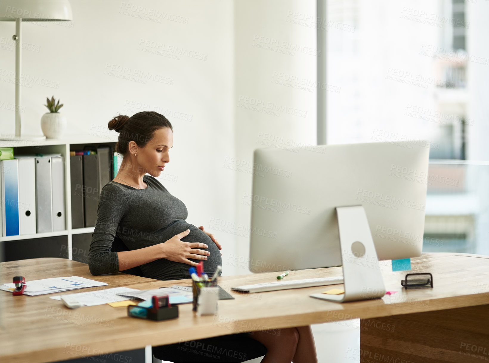 Buy stock photo Shot of a pregnant businesswoman sitting at her office desk holding her stomach