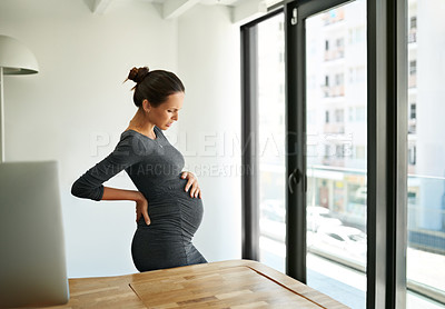 Buy stock photo Shot of a pregnant businesswoman standing in her office holding her stomach