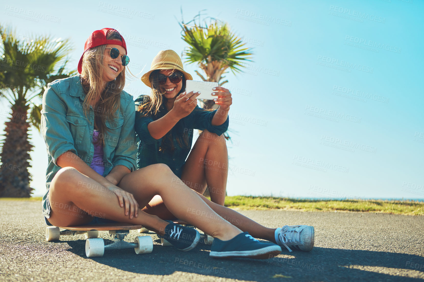 Buy stock photo Shot of two friends hanging out on the boardwalk with a skateboard