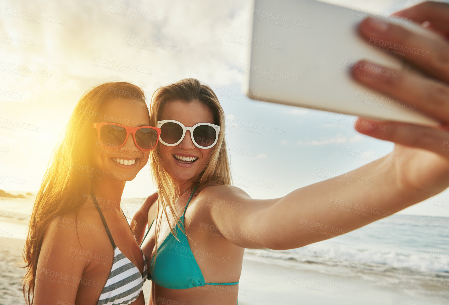 Buy stock photo Shot of two friends taking selfies while hanging out at the beach