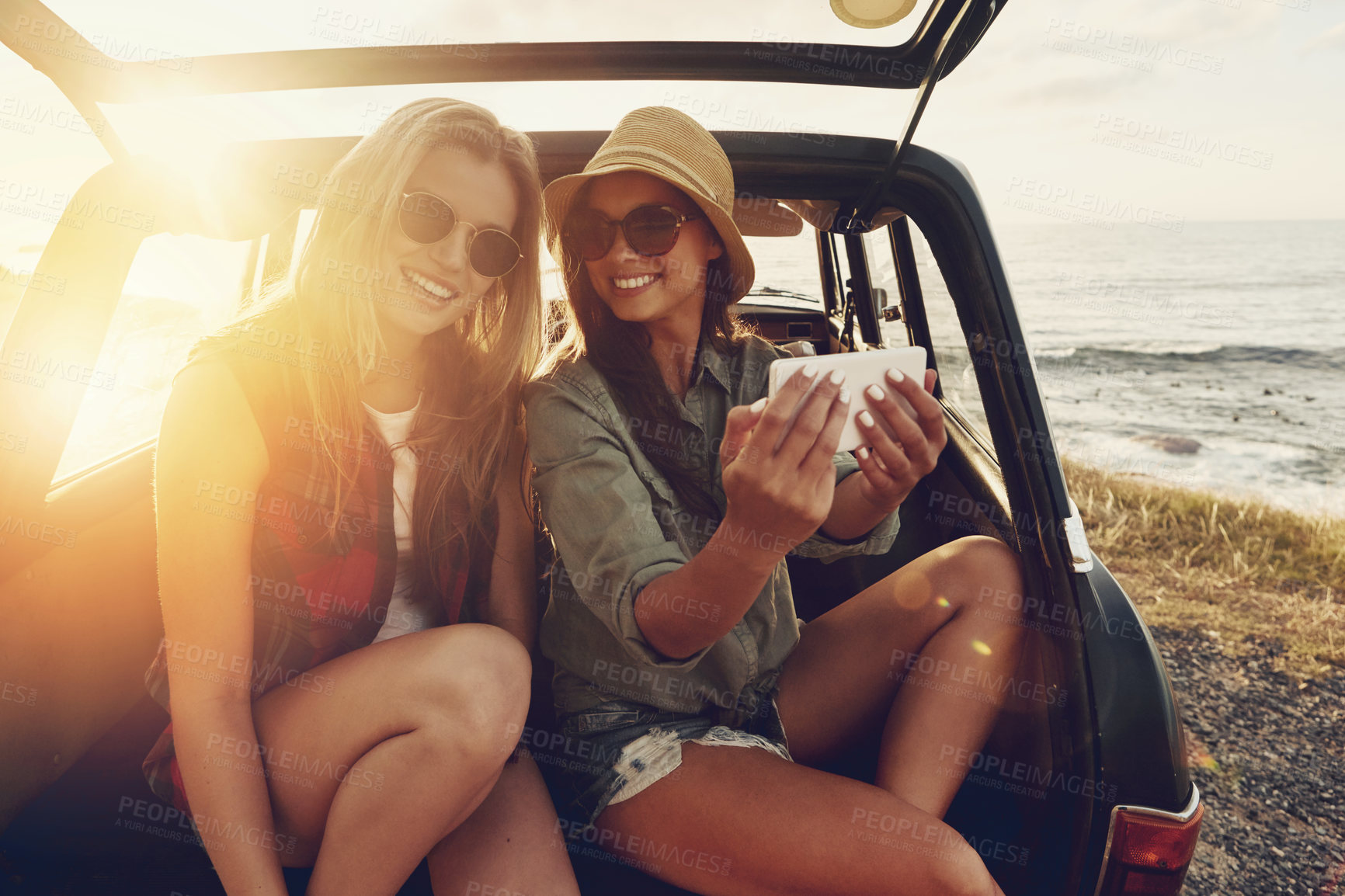 Buy stock photo Beach, women and selfie at sunset for road trip and adventure in car for outdoor memory and holiday. Ocean, girl friends or happy people in picture on fun summer vacation, photography and lens flare