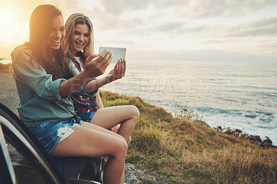 Buy stock photo Cropped shot of two friends taking a selfie while sitting on the hood of a car