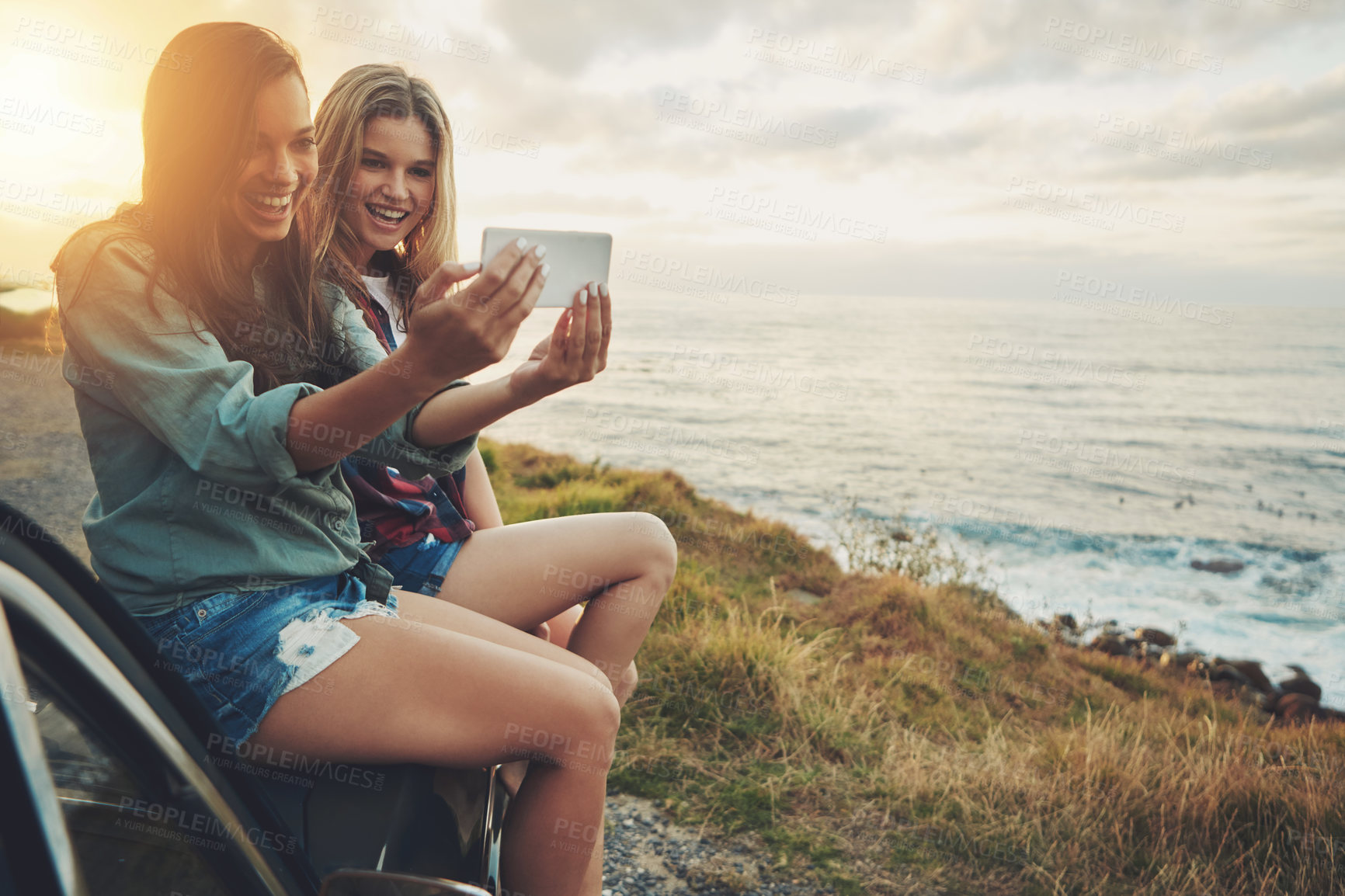 Buy stock photo Cropped shot of two friends taking a selfie while sitting on the hood of a car