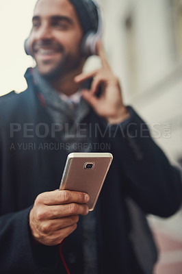 Buy stock photo Cropped shot of a fashionable young man listening to music on his phone while out in the city
