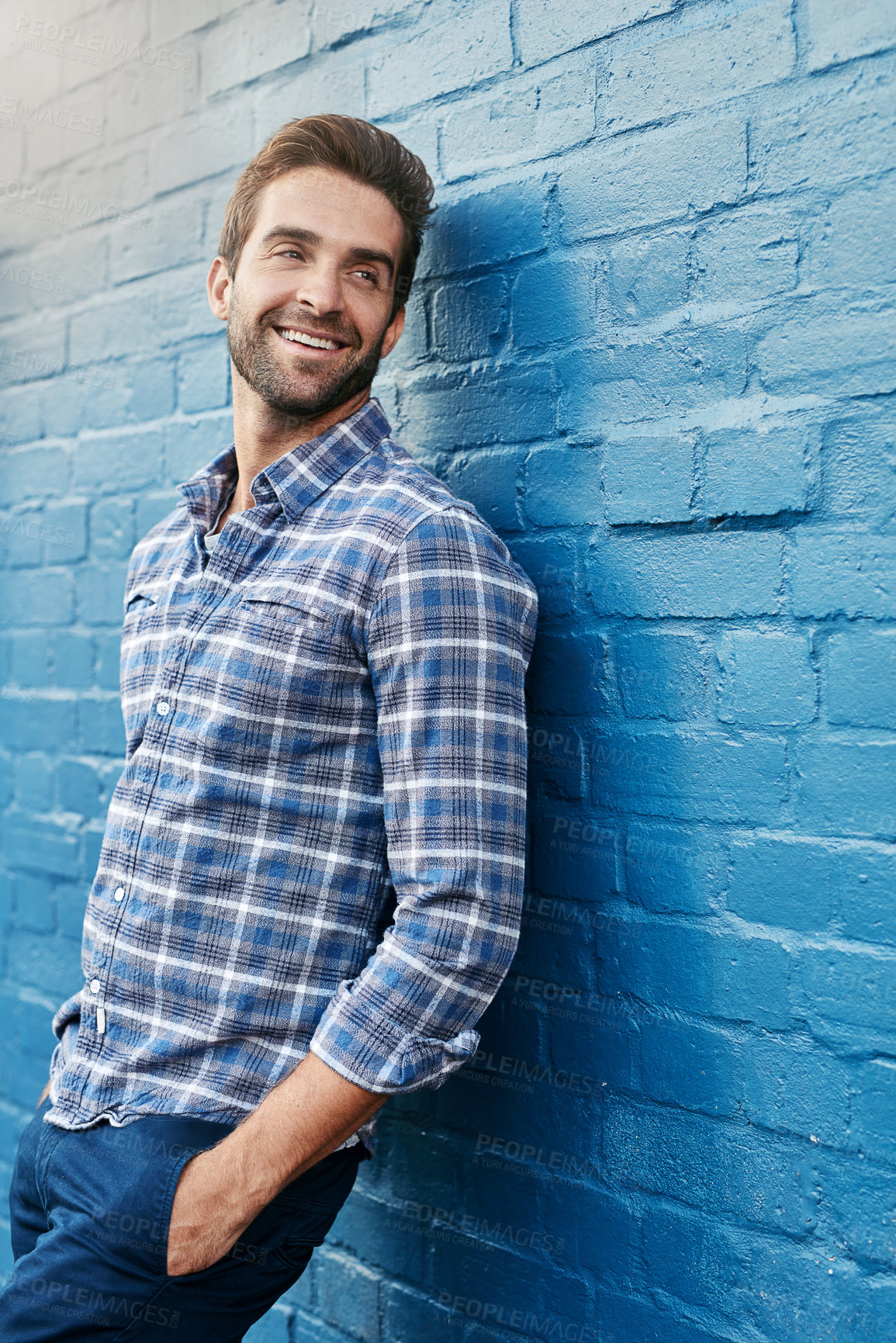 Buy stock photo Shot of a handsome young man leaning against a wall