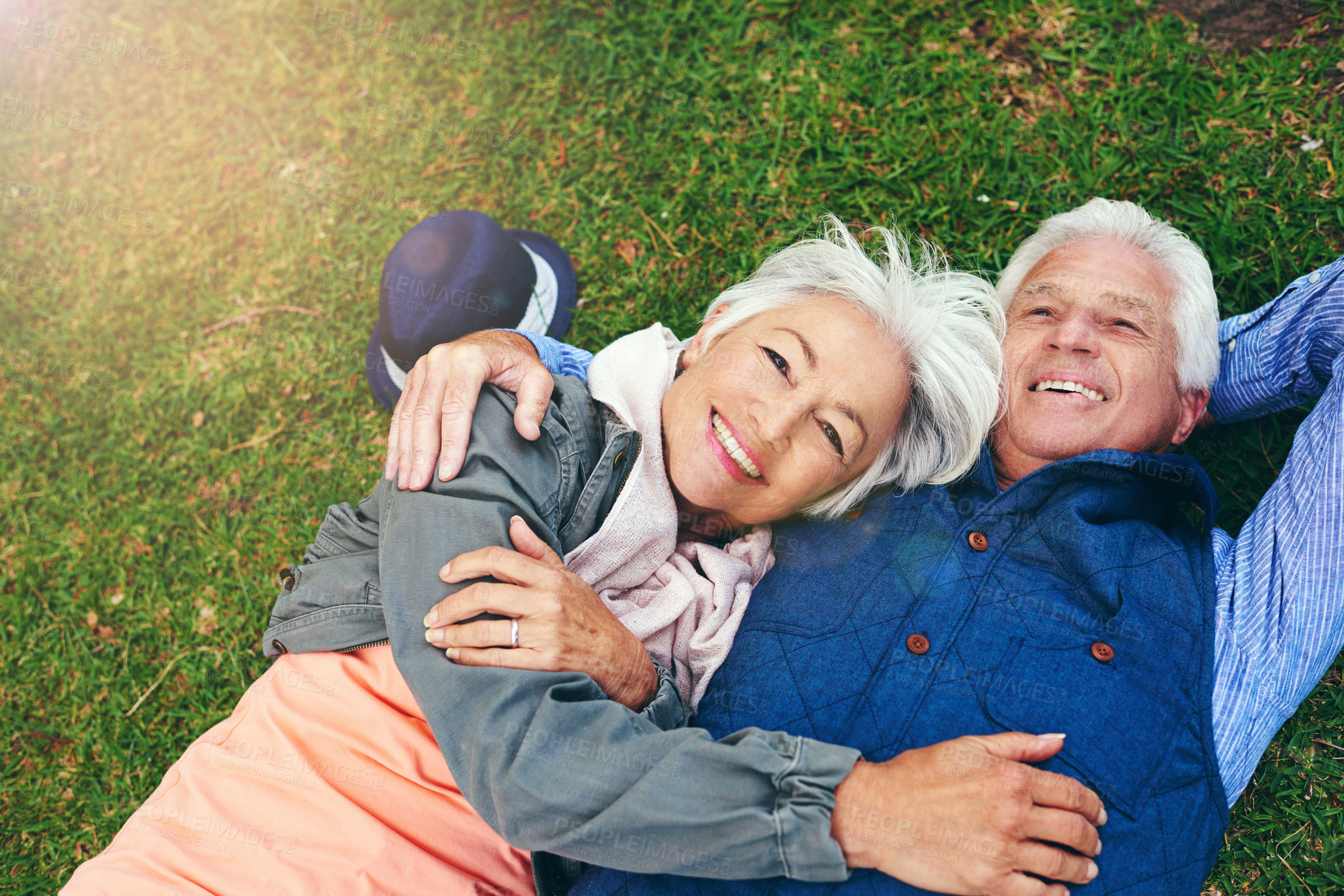 Buy stock photo Portrait of a happy senior couple lying down on the grass together in the park