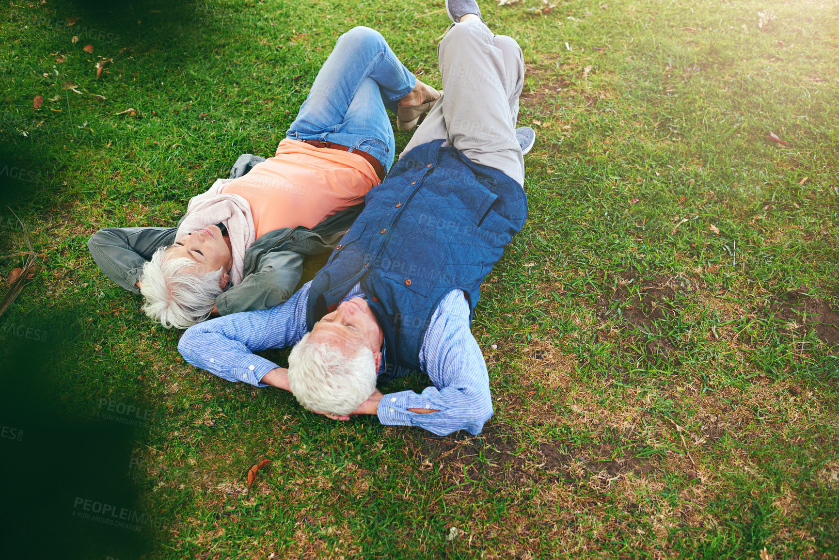 Buy stock photo Shot of a senior couple lying down on the grass and looking up at the sky