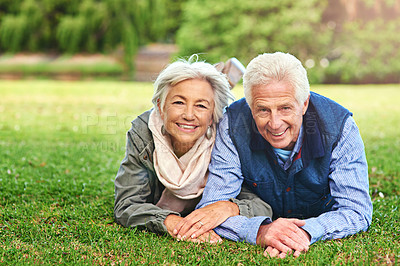 Buy stock photo Portrait of a happy senior couple lying down on the grass together in the park