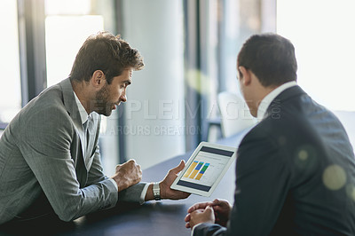 Buy stock photo Shot of two colleagues looking at a graph on a digital tablet together in an office