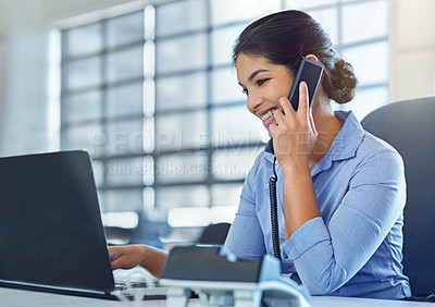 Buy stock photo Shot of a young businesswoman talking on the phone while using a laptop at work
