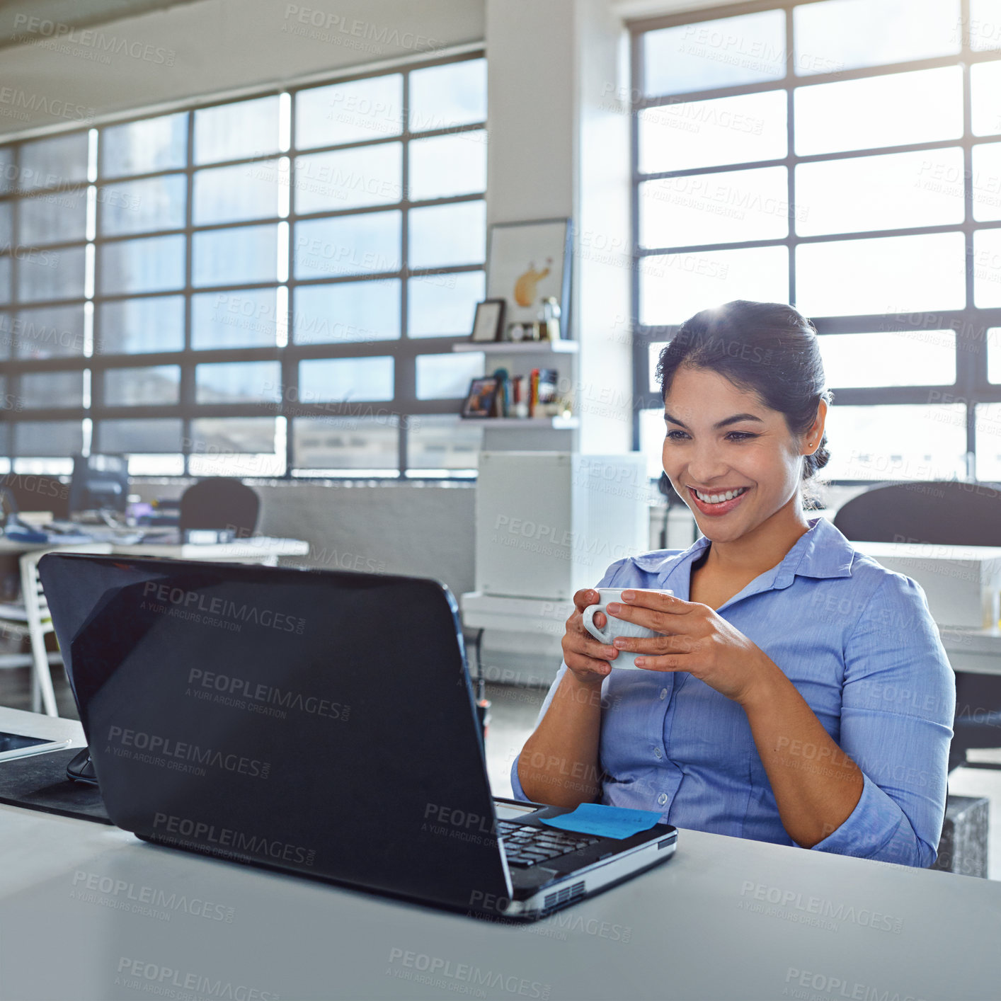 Buy stock photo Shot of a young businesswoman drinking a beverage while using a laptop at work