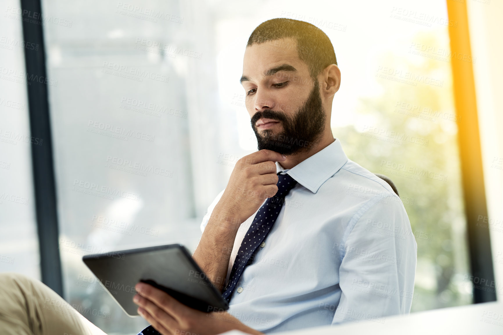 Buy stock photo Shot of a young businessman using a digital tablet at his desk in an office