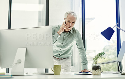 Buy stock photo Shot of a mature businessman talking on the phone while working standing at his desk in an office