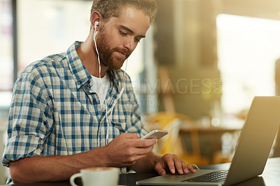 Buy stock photo Shot of a young man with earphones using a cellphone and laptop in a cafe
