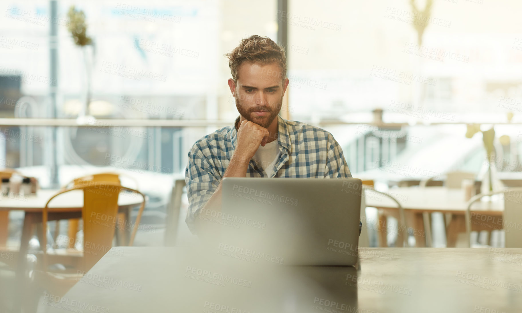 Buy stock photo Shot of a young man using a laptop in a cafe