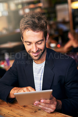 Buy stock photo Shot of a handsome young man using a digital tablet in a cafe