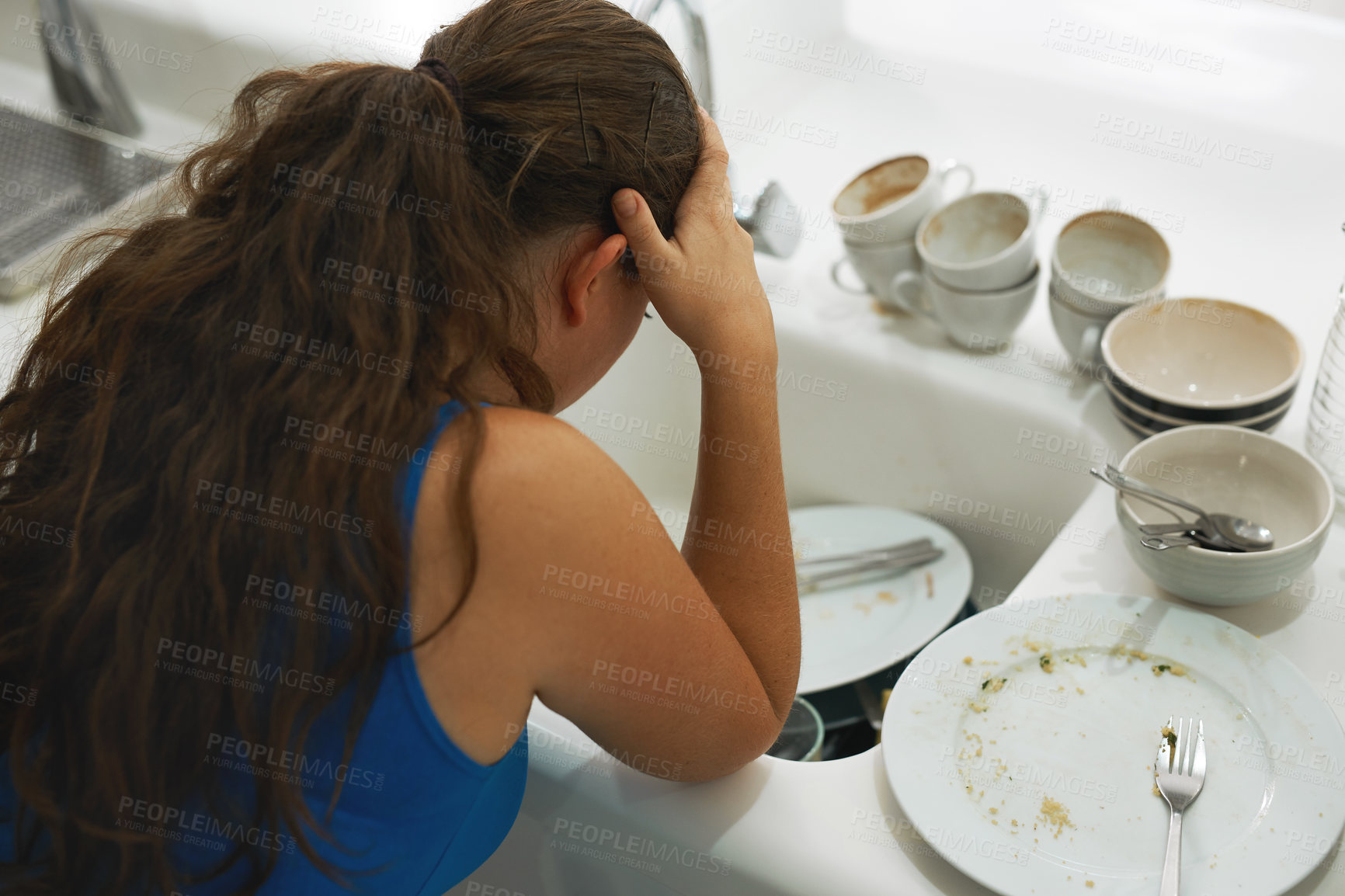 Buy stock photo Shot of a frustrated looking woman standing by a pile of dirty dishes