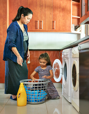 Buy stock photo Shot of a pregnant mother and daughter using a washing machine at home