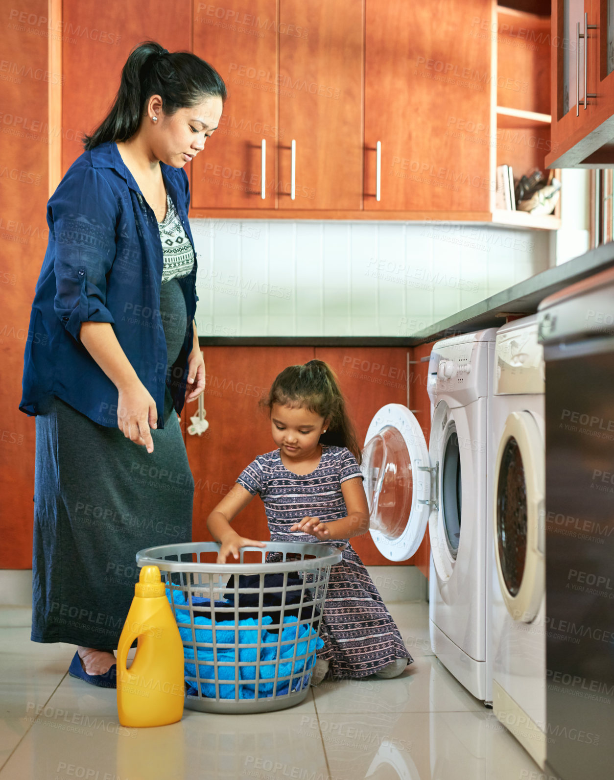 Buy stock photo Shot of a pregnant mother and daughter using a washing machine at home