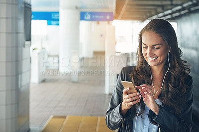 Buy stock photo Shot of a young woman listening to music on a phone in an urban setting