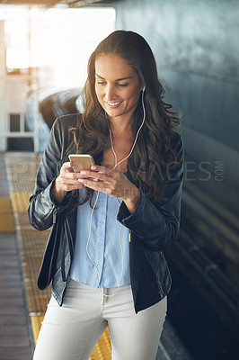 Buy stock photo Shot of a young woman listening to music on a phone in an urban setting