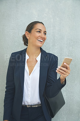 Buy stock photo Shot of a young businesswoman using her phone while standing against a gray wall