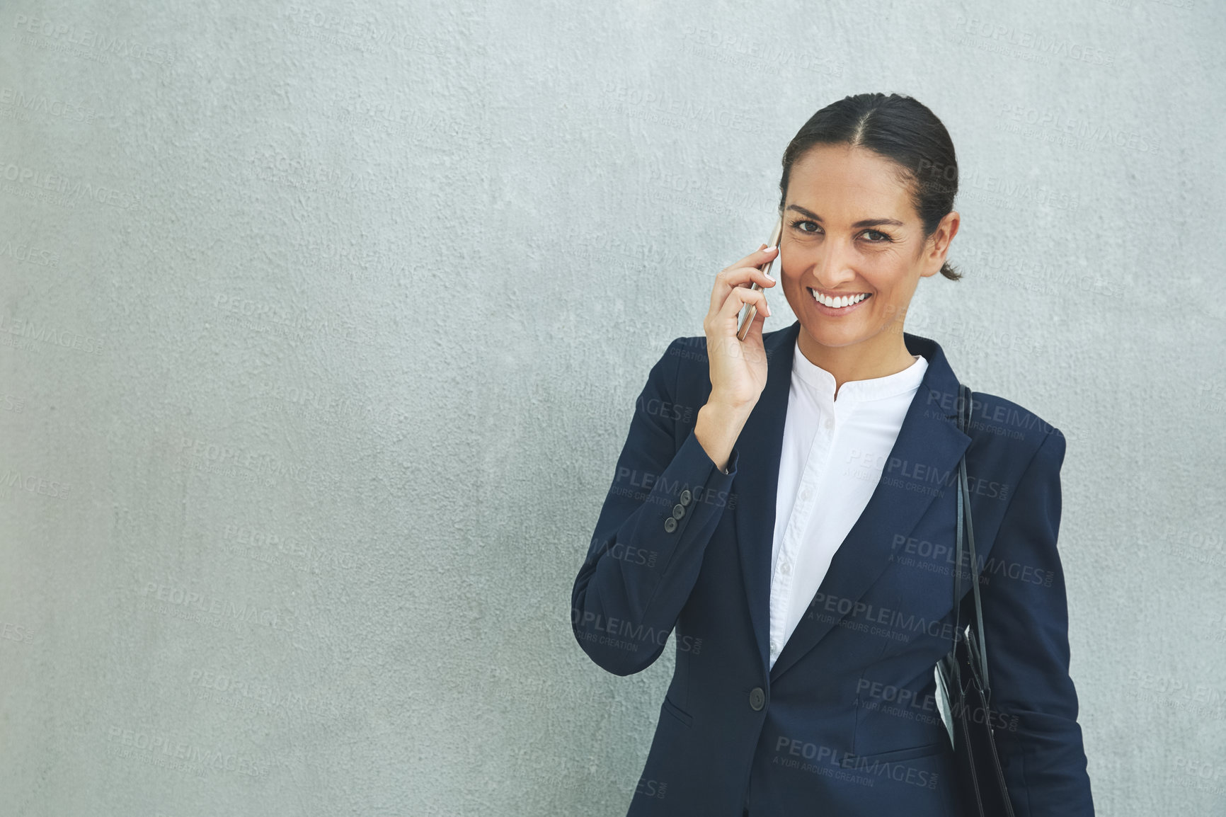 Buy stock photo Portrait of a young businesswoman using her phone while standing against a gray wall