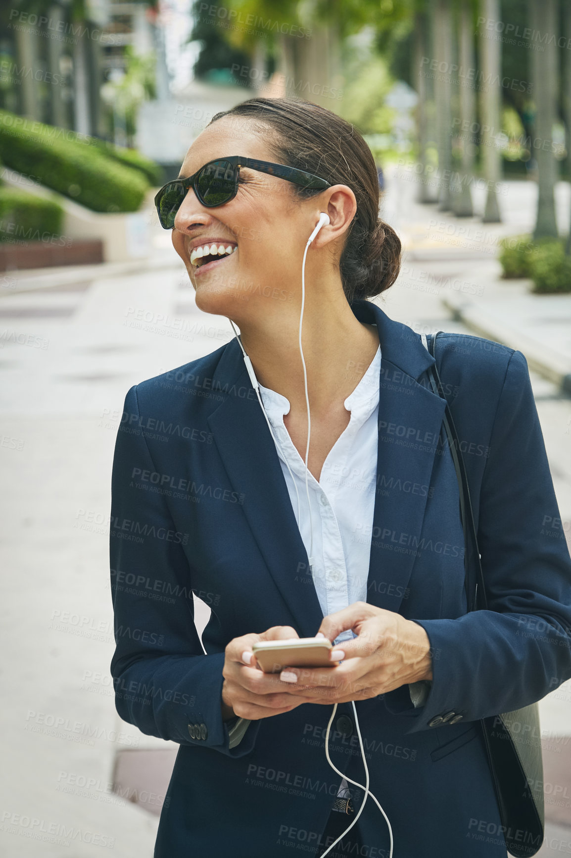 Buy stock photo Shot of a young businesswoman her phone and earphones while out in the city