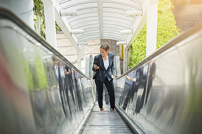 Buy stock photo Shot of a young businesswoman using a cellphone on an escalator