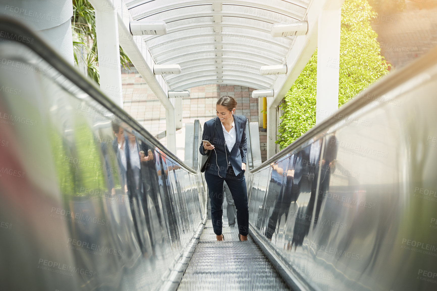 Buy stock photo Shot of a young businesswoman using a cellphone on an escalator