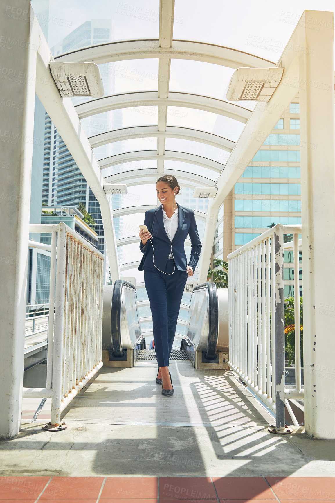 Buy stock photo Shot of a young businesswoman using a cellphone while getting off an escalator