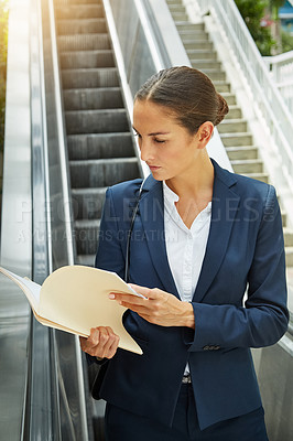 Buy stock photo Shot of a young businesswoman reading paperwork on an escalator