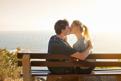 Buy stock photo Shot of a loving couple sitting on a bench overlooking the ocean