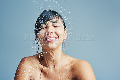 Buy stock photo Shot of a young woman having a refreshing shower against a blue background