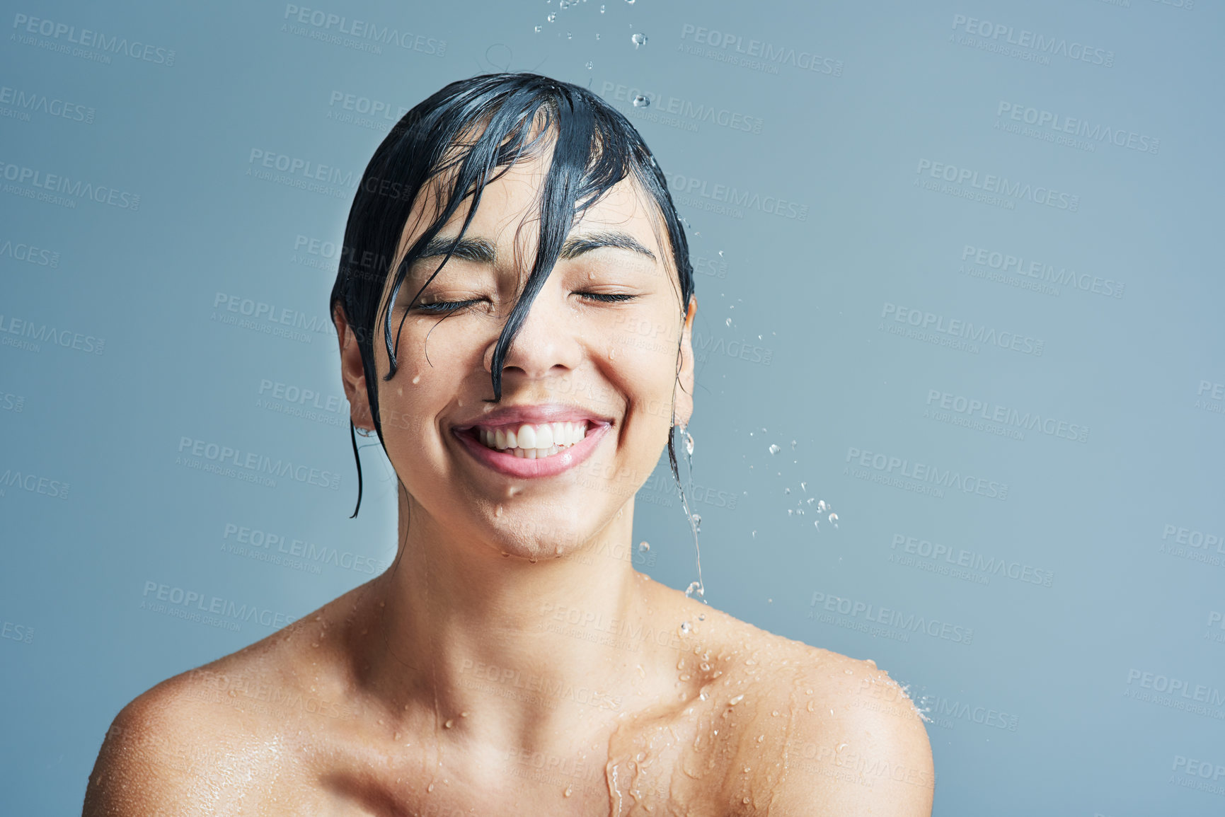 Buy stock photo Beauty, water splash and face of woman shower on blue background for wellness, cleaning and grooming. Skincare, bathroom and happy female person for washing hair, body care and cleansing in studio