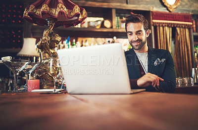 Buy stock photo Cropped shot of a young man using his laptop while sitting in a bar