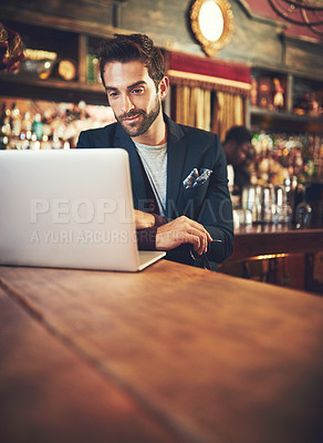 Buy stock photo Cropped shot of a young man using his laptop while sitting in a bar