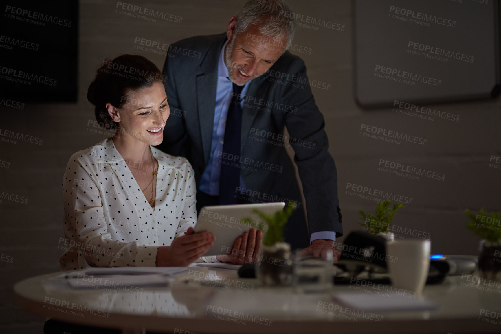 Buy stock photo Shot of two colleagues using a digital tablet while working late in an office
